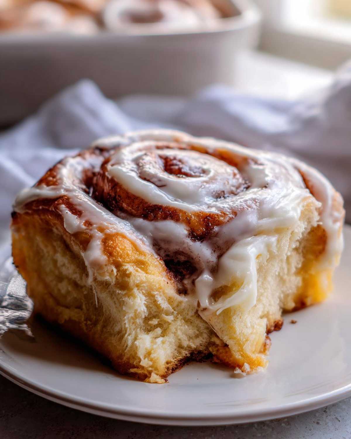 Close-up of a soft, fluffy cinnamon roll topped with dripping white cream cheese icing, showing the swirl pattern.