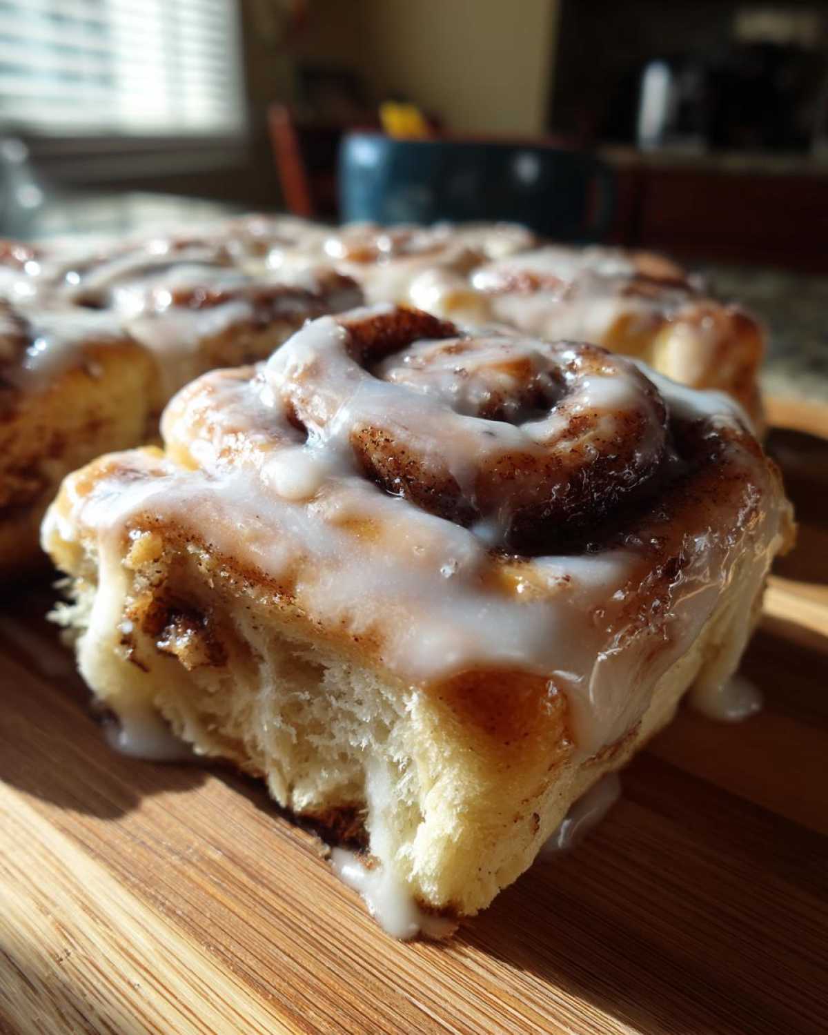 A close-up, sunlit view of a soft, fluffy cinnamon roll topped with thick white icing.