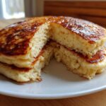 Close-up of fluffy coconut flour pancakes stacked and cut in half, showing the airy interior and golden syrup topping.