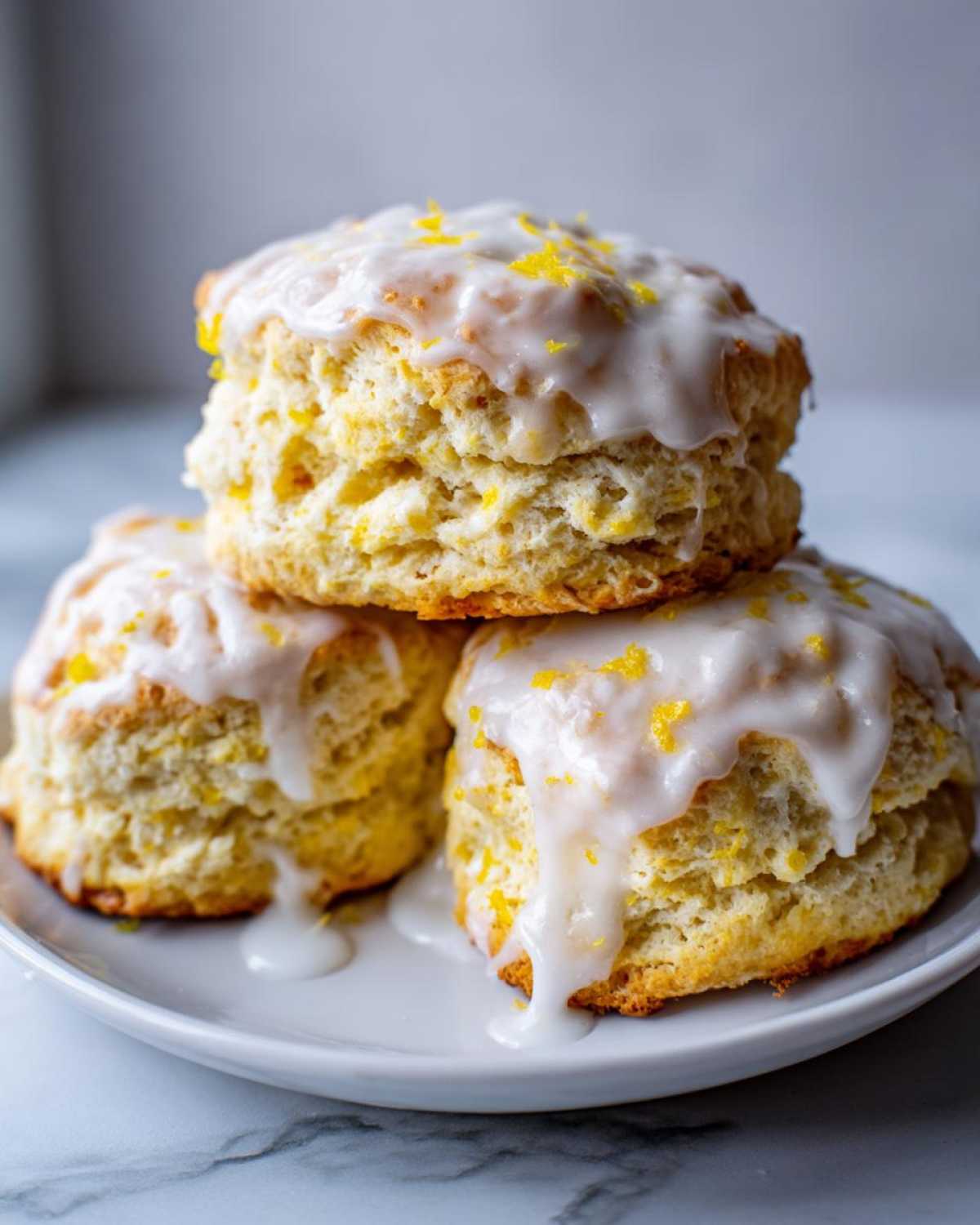 A stack of three fluffy lemon scones topped with thick white glaze and bright yellow lemon zest.