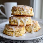 A stack of three fluffy lemon scones generously topped with a white lemon glaze, served on a white plate.