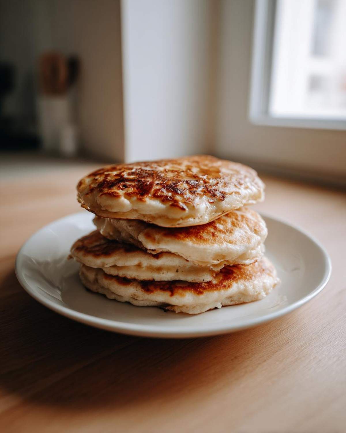 A stack of four thick, fluffy sourdough pancakes with golden-brown edges served on a white plate.