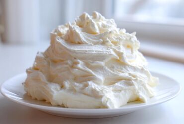 A generous mound of fluffy, perfectly piped vanilla buttercream frosting sitting on a small white plate.