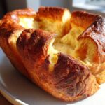 A golden brown, perfectly risen yorkshire pudding with a crisp exterior and soft interior, sitting on a light plate.