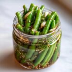 Close-up of bright green dilly beans packed tightly in a glass jar with dill, garlic, and pickling spices.