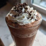 Close-up of a tall glass of frozen hot chocolate topped with whipped cream and chocolate shavings.