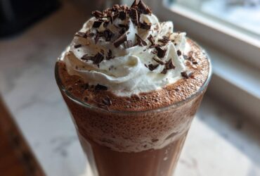 Close-up of a tall glass of frozen hot chocolate topped with whipped cream and chocolate shavings.