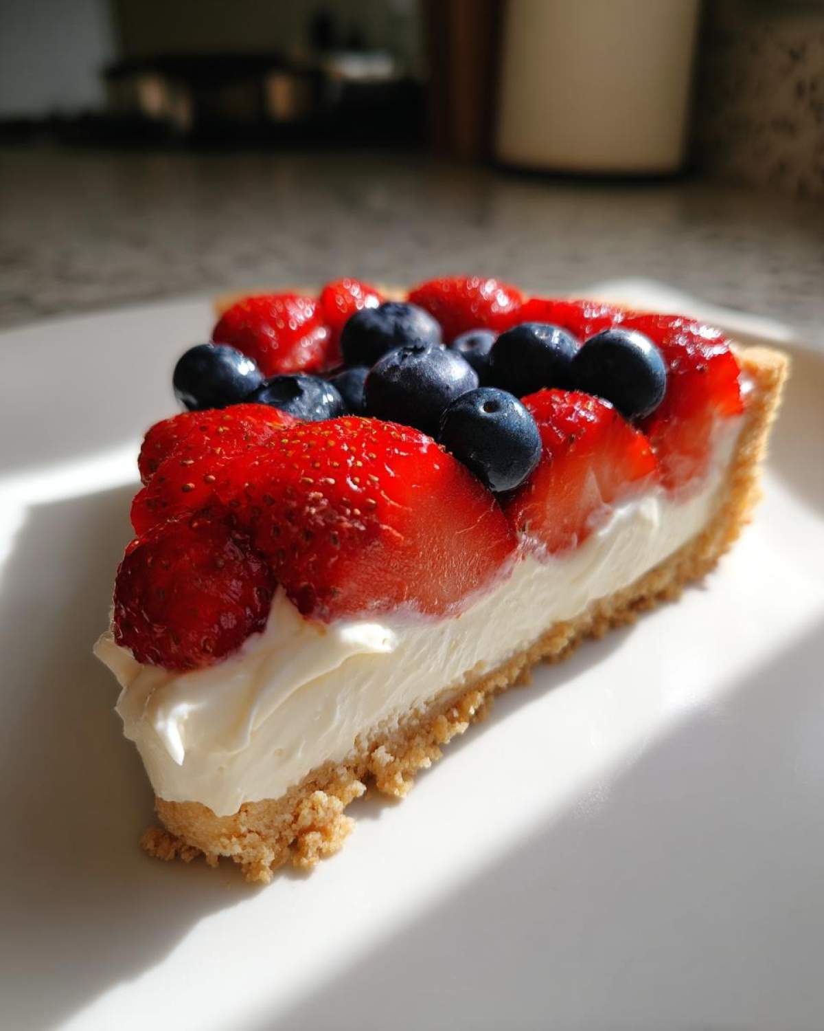 Close-up of a slice of fruit pizza sugar cookie topped with cream cheese frosting, strawberries, and blueberries.