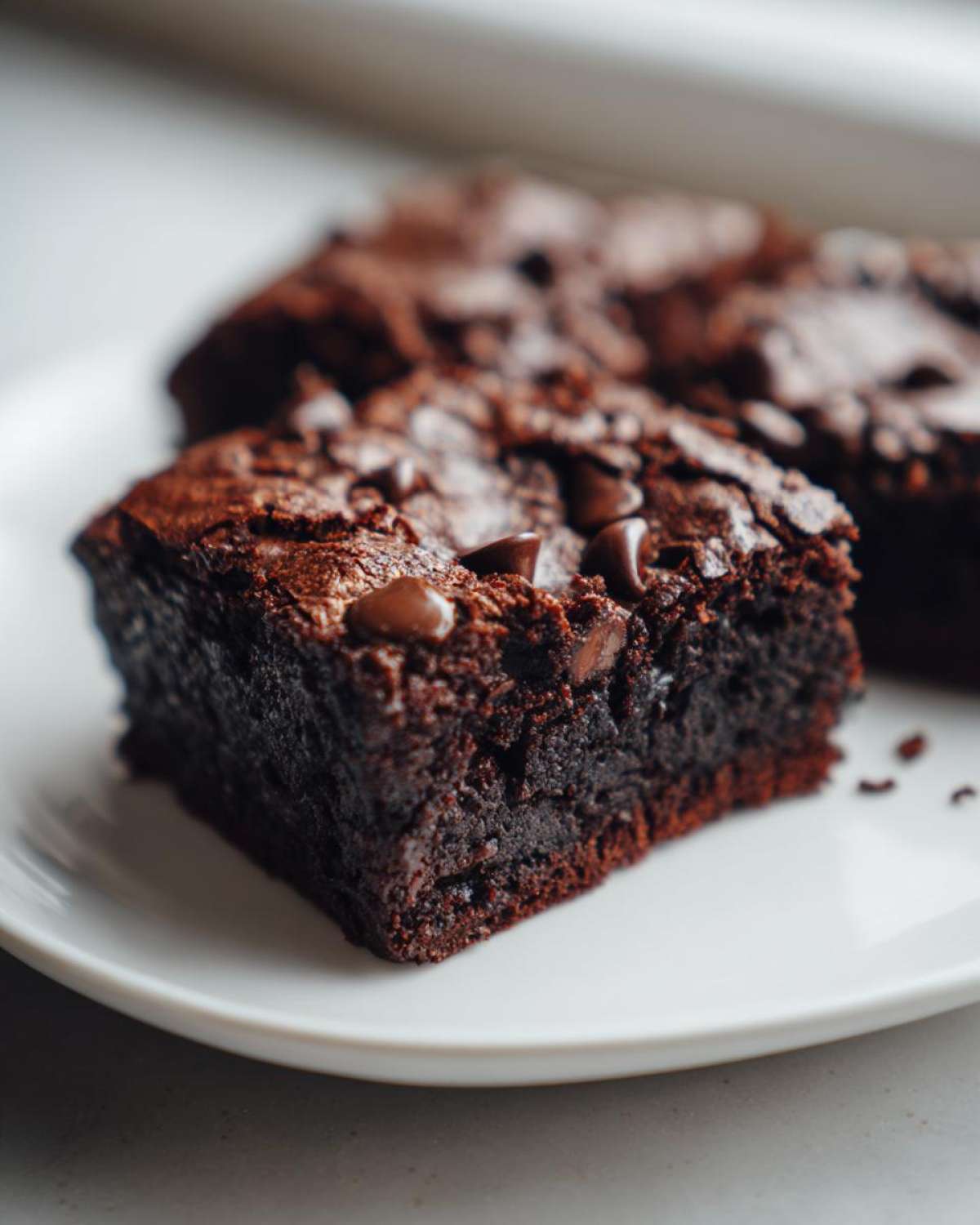 Close-up of a fudgy square of sweet potato brownies topped with melted chocolate chips on a white plate.