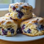 A stack of three freshly baked blueberry scones topped with a sweet white glaze.