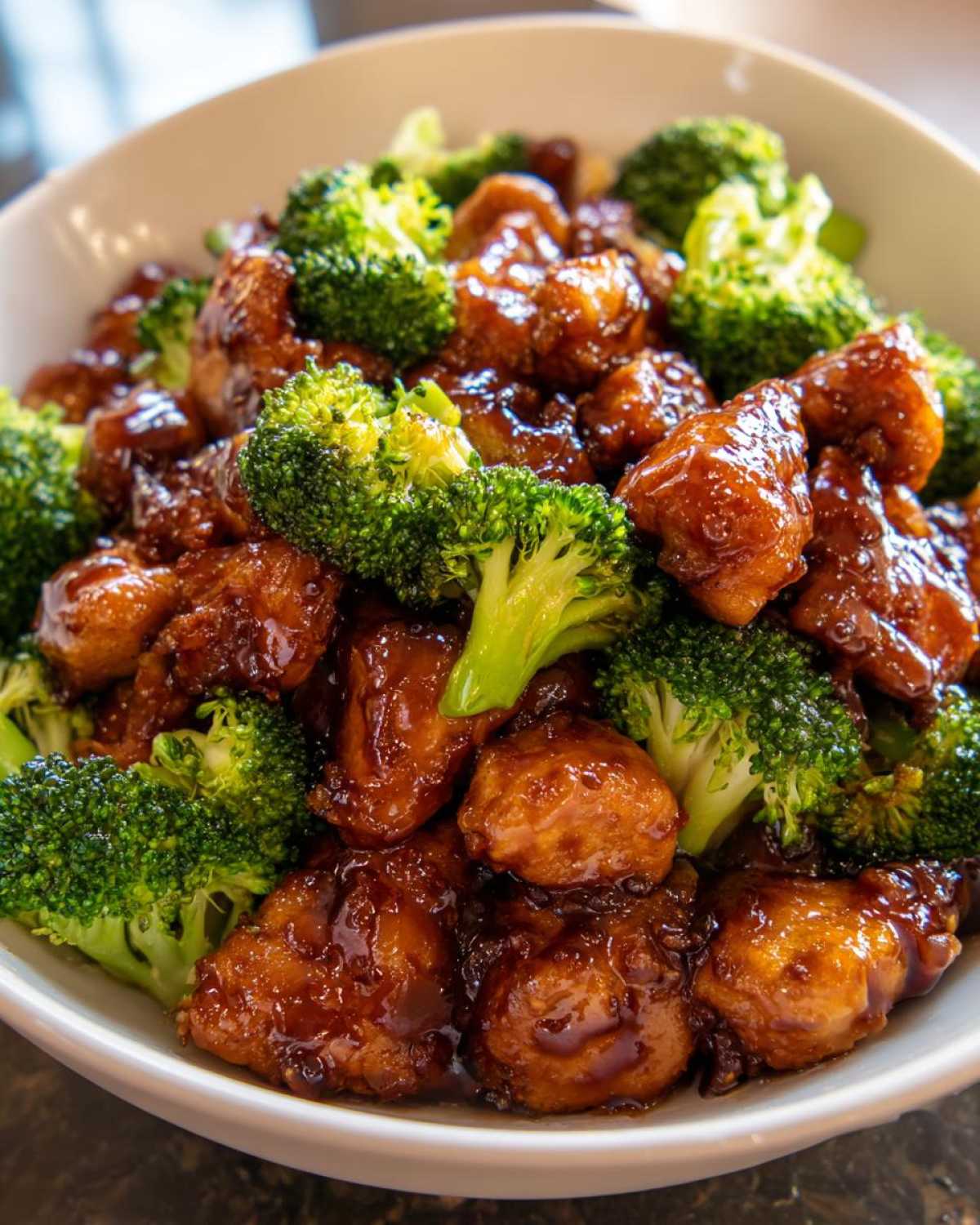 Close-up of tender, saucy chicken and bright green broccoli florets in a white bowl, showcasing the chicken and broccoli dish.