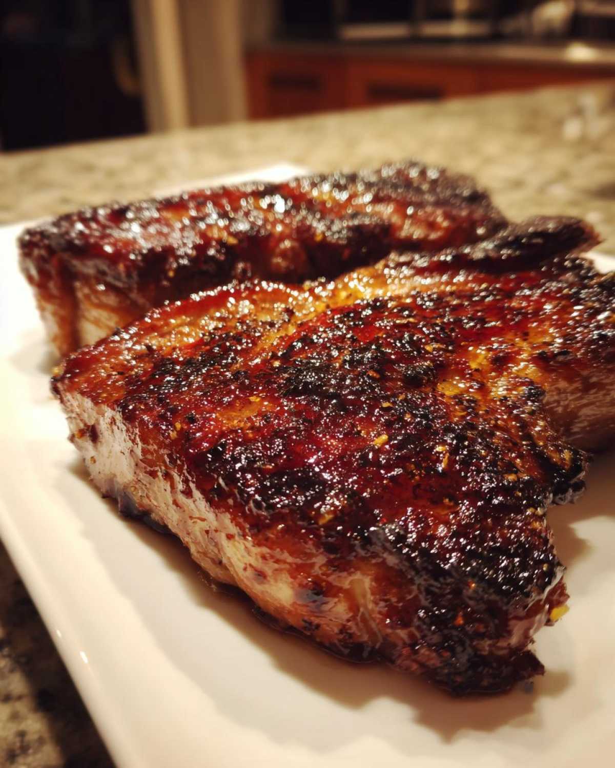 Close-up of two thick, glazed, and perfectly seared pieces of pork steak resting on a white plate.