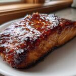 Close-up of a perfectly cooked salmon fillet with a dark, glossy glaze served on a white plate.