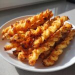 A pile of golden, flaky, twisted cheese straws recipe baked until crispy, served on a white plate.