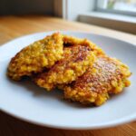 Three golden brown, crispy fried cornbread patties stacked slightly on a white plate.