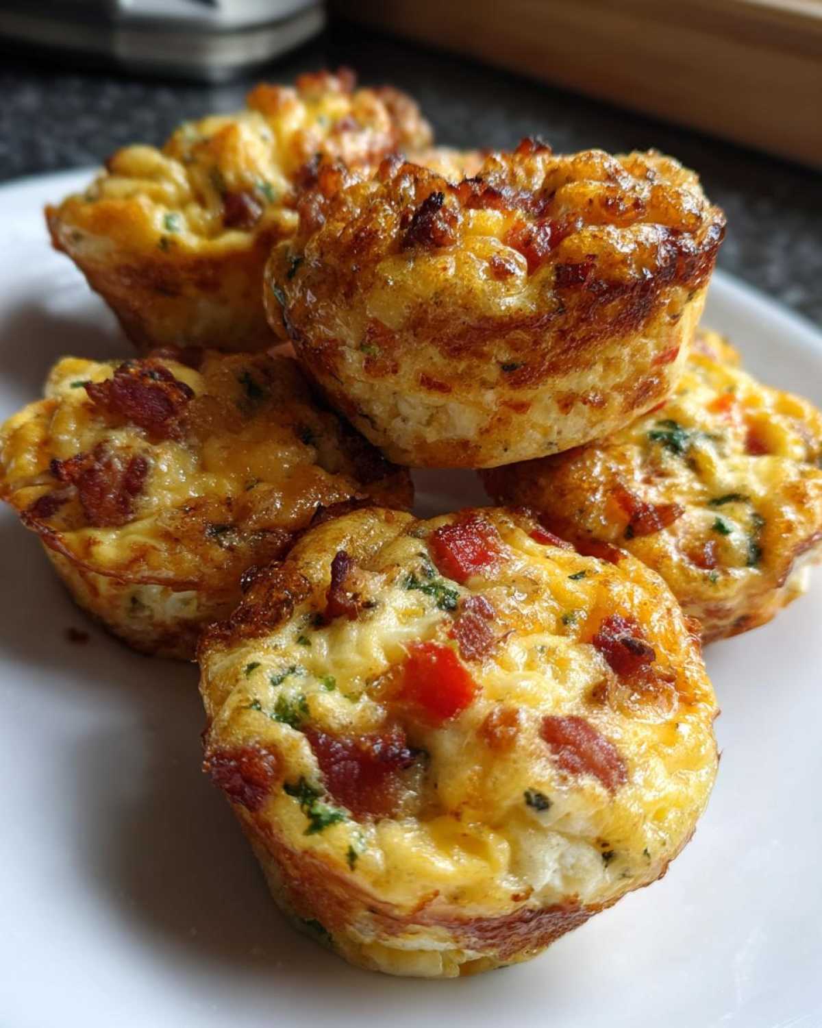 A stack of five golden brown muffin tin egg bites, filled with bacon and peppers, resting on a white plate.