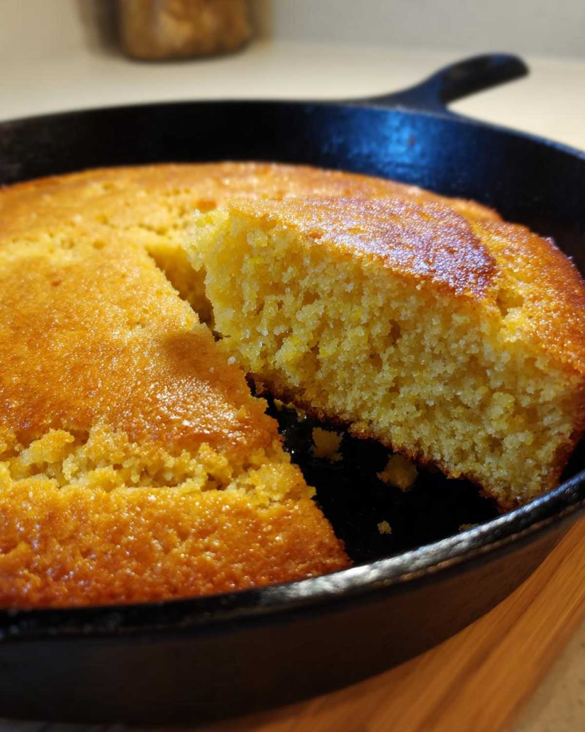 A close-up of golden brown skillet cornbread with one slice partially lifted out, showing the crumb texture.