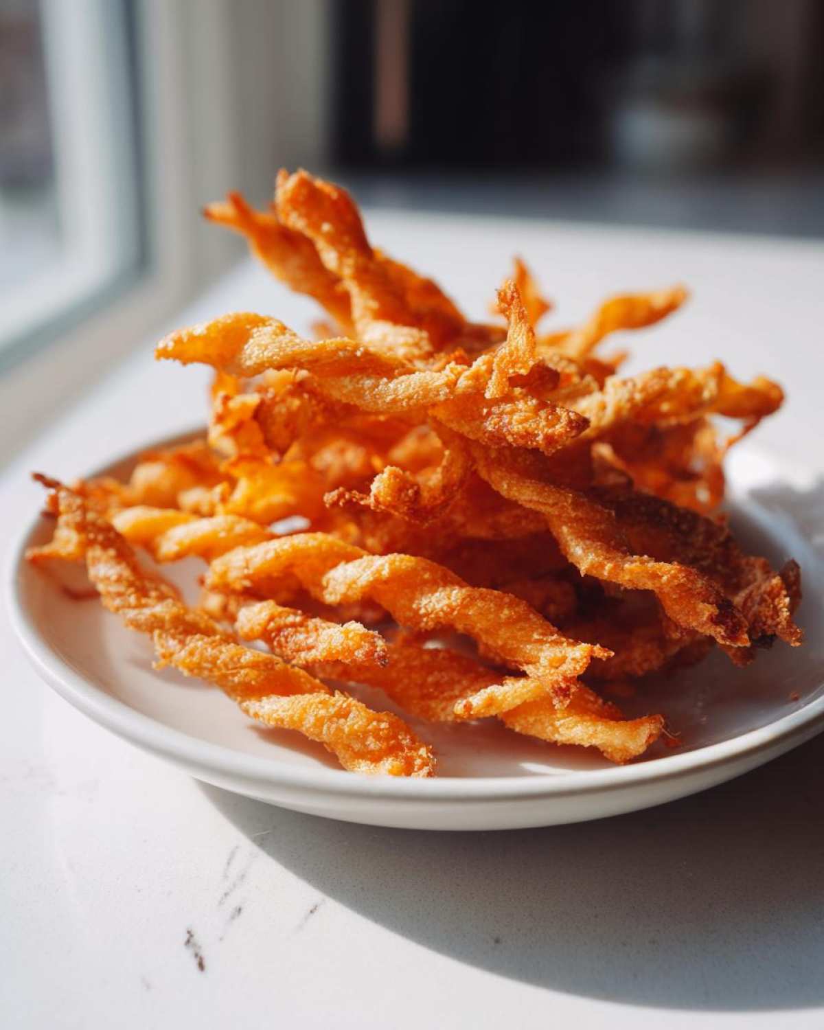A pile of golden brown, crispy, twisted cheese straws recipe served on a small white plate.