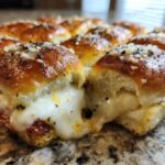 Close-up of gooey pizza sliders showing melted cheese pulling apart between baked rolls, topped with seasoning.
