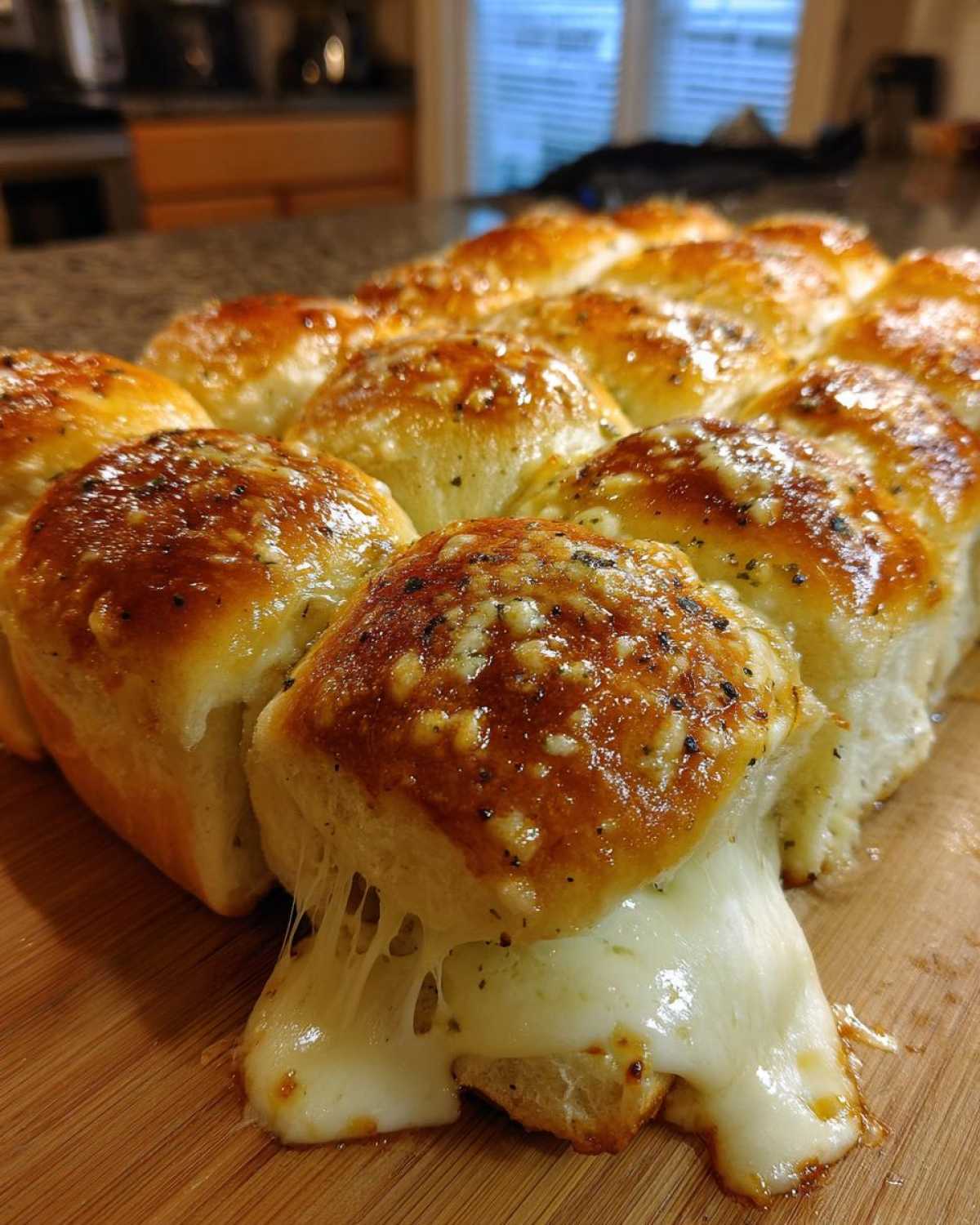 Close-up of freshly baked pizza sliders with melted cheese stretching out, topped with garlic butter and herbs.