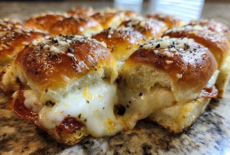 Close-up of gooey pizza sliders showing melted cheese pulling apart between baked rolls, topped with seasoning.