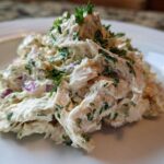 Close-up of a scoop of creamy greek yogurt chicken salad mixed with red onion and fresh parsley.