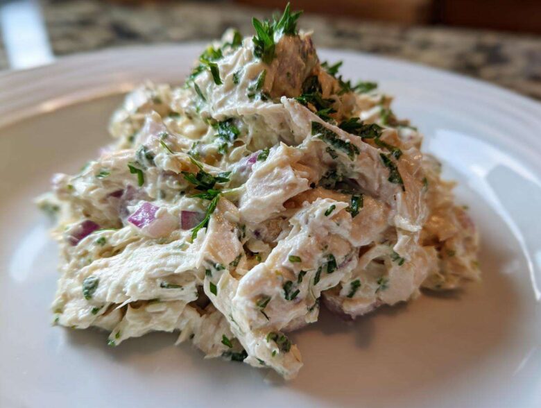 Close-up of a scoop of creamy greek yogurt chicken salad mixed with red onion and fresh parsley.