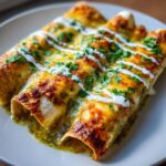 Close-up of baked green chile chicken enchiladas covered in melted cheese, sour cream drizzle, and fresh cilantro.