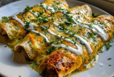 Three baked green chile chicken enchiladas covered in melted cheese, sour cream drizzle, and fresh cilantro.