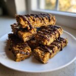 A stack of homemade, chewy protein bars drizzled generously with melted dark chocolate.