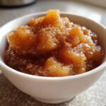 Close-up of chunky, spiced homemade applesauce in a small white bowl, dusted with cinnamon.