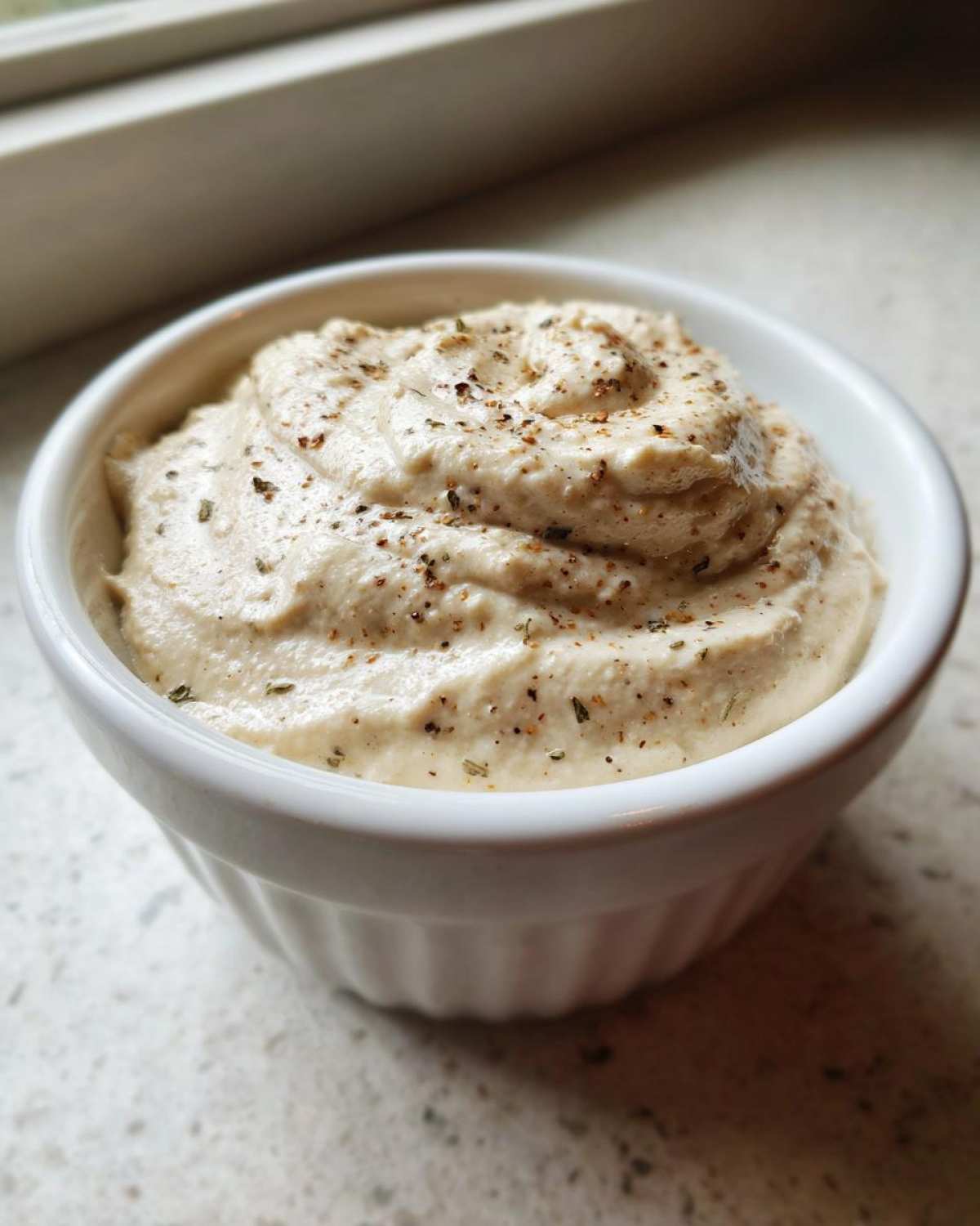 Close-up of a small white bowl filled with a thick, creamy mixture, likely homemade cream of chicken soup base, topped with pepper.