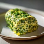 A log of homemade garlic butter mixed with green herbs, resting on a light ceramic plate.
