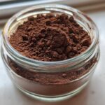Close-up of rich, dark brown homemade hot cocoa mix filling a small, clear glass jar.