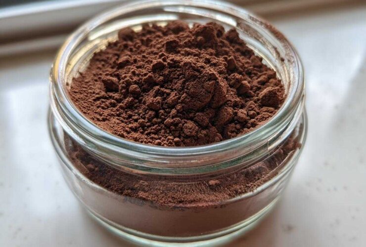 Close-up of rich, dark brown homemade hot cocoa mix filling a small, clear glass jar.
