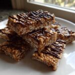 A stack of homemade, chewy protein bars made with oats and drizzled with dark chocolate, ready to eat.