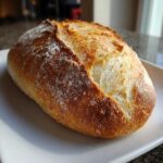 Close-up of a rustic, golden-brown loaf of homemade italian bread resting on a white plate.
