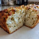 A loaf of amazing Italian herb and cheese bread, sliced open to show melted cheese pockets and green herbs inside.