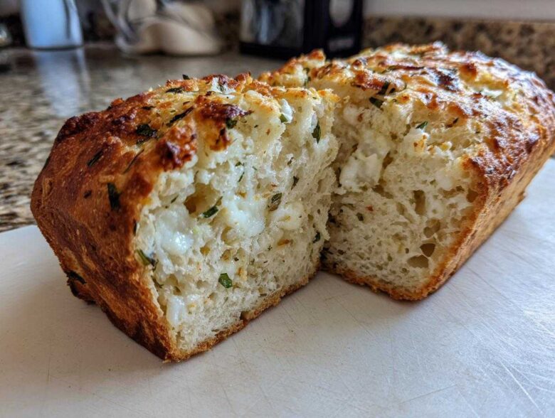 A loaf of amazing Italian herb and cheese bread, sliced open to show melted cheese pockets and green herbs inside.