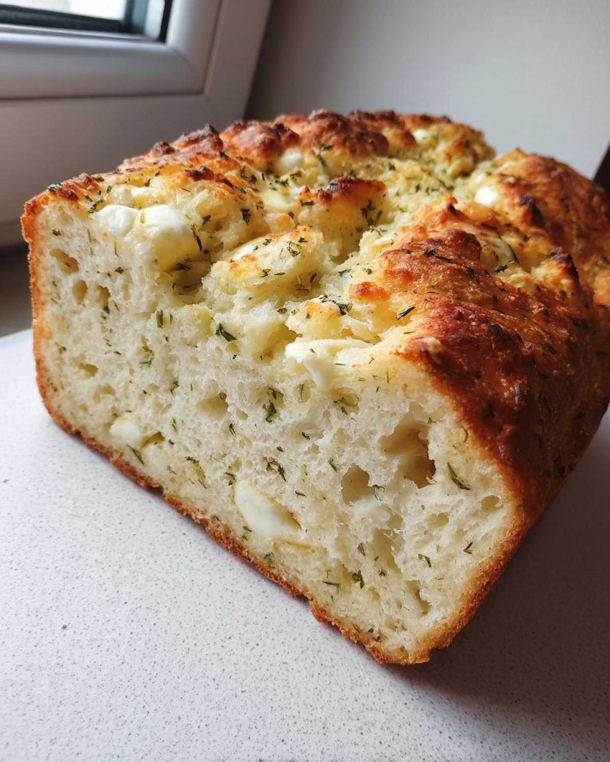 Close-up of a freshly baked Italian herb and cheese bread loaf, showing the soft interior with visible cheese chunks and herbs.