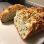 Close-up of a freshly baked Italian herb and cheese bread, showing its airy interior and cheesy, herbed crust.