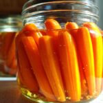 Close-up of whole baby carrots tightly packed in a glass jar for pickled carrots, submerged in brine.