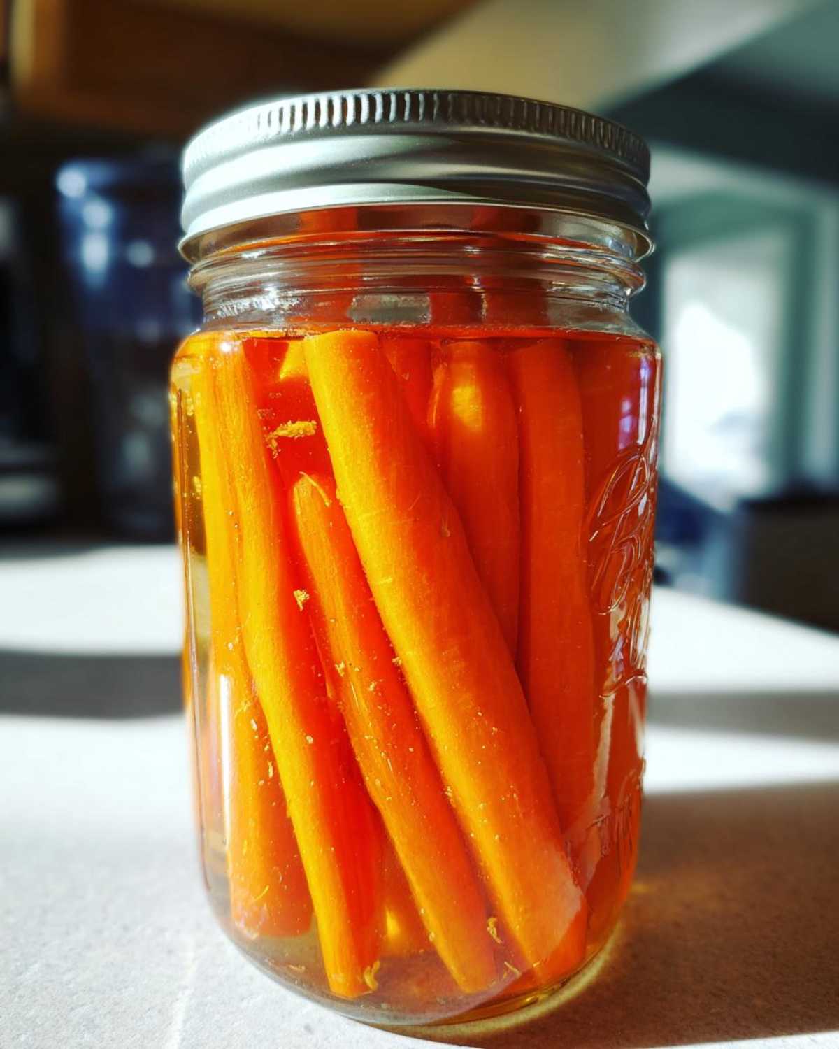 Close-up of bright orange carrot sticks submerged in liquid inside a mason jar, showcasing the pickled carrots.