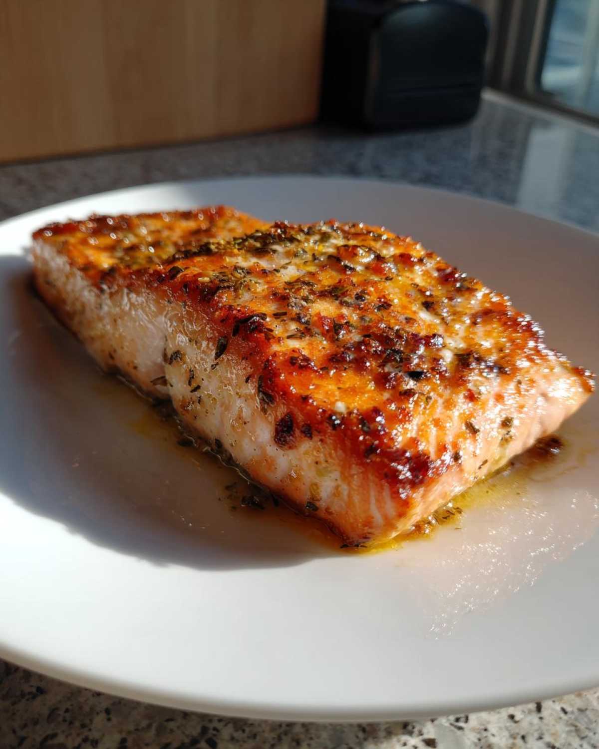 Close-up of a juicy, seasoned air fryer salmon fillet resting on a white plate.