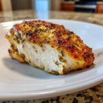 Cross-section of a juicy baked chicken breast seasoned with herbs, showing white meat and a golden-brown crust.
