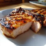 Close-up of a thick, juicy grilled pork chop showing grill marks and a glistening marinade for pork chops.