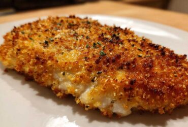 A close-up, golden-brown piece of parmesan crusted chicken showing a crispy coating and juicy white meat underneath.