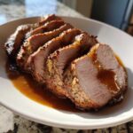 Slices of perfectly cooked pork loin roast, seasoned and drizzled with brown gravy, served on a white plate.