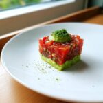 A square tower of vibrant tuna tartare layered over avocado puree, topped with more avocado and fine green herbs.