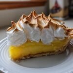 A perfect slice of lemon meringue pie showing bright yellow filling and high, toasted meringue peaks.